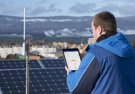 A technician in front of a LORIX One on a mast and using a tablet to configure the gateway via its web interface.